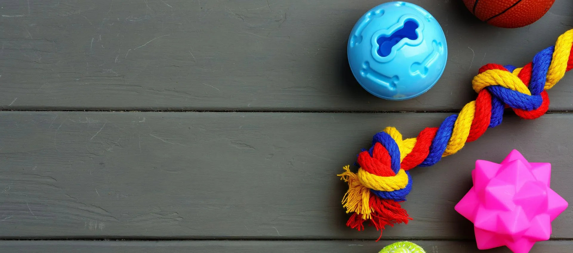 Hundespielzeuge wie Seilknoten, Ball und Kauspielzeug auf einer grauen Holzfläche.