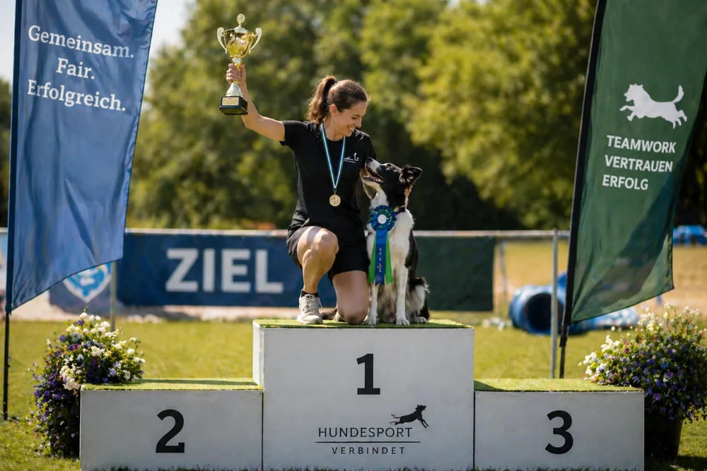 Frau und Hund stehen gemeinsam auf dem ersten Platz bei einer Siegerehrung im Hundesport – Symbol für langfristigen Erfolg, Teamarbeit und Vertrauen.
